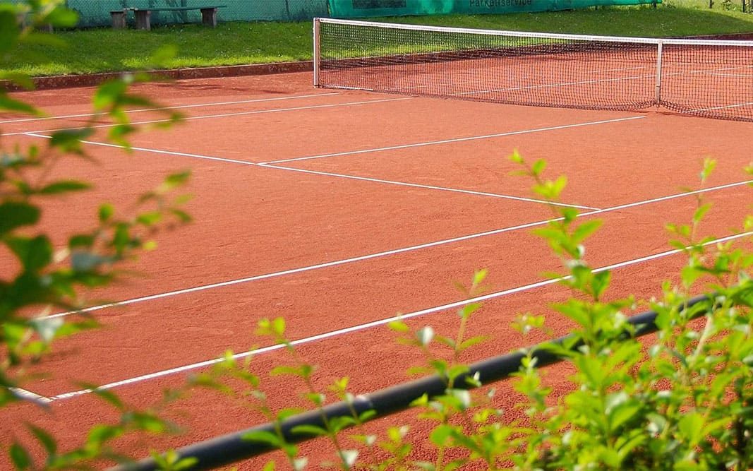 Sandplatz mit Netz, gesehen durch Grün am Platzrand